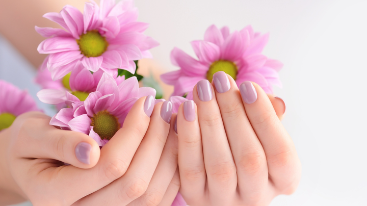 A person holding spring pink flowers in their hands with their bails painted in trending 2023 spring nail colors.