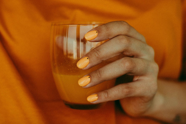 A person dressed in orange and holding a glass of orange juice with orange nail polish on to help affect their mood.