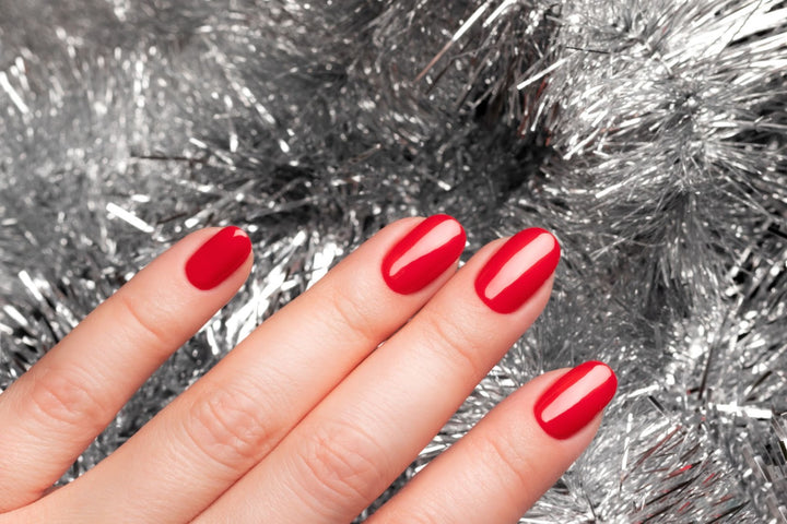 Person showing off their red painted nails on a silver holiday background from a liberation nails non-toxic nail polish gift.