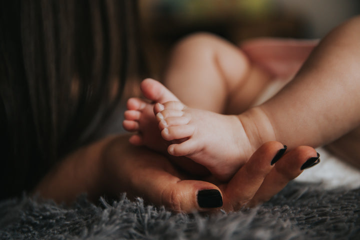 Close up shot of mother's hand with black nail polish holding her baby's feet in her hands 