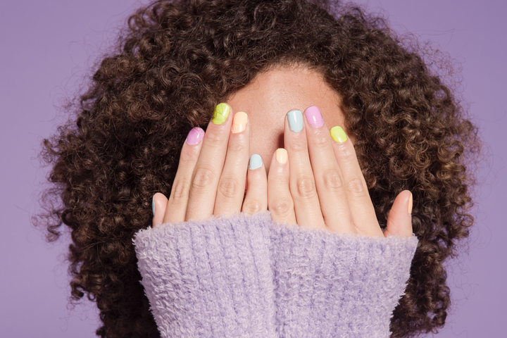A person holding up her hands over her face to show the best spring nail colors for 2023 on her nails.